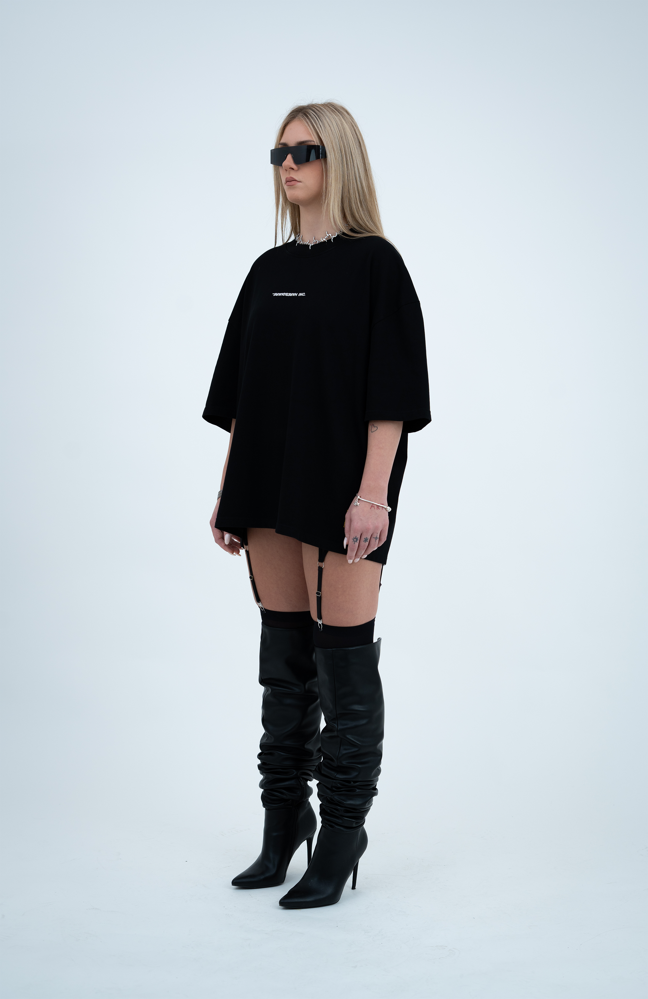 Model in the Haresquare Black T-shirt with a white print, styled with Haresquare mini skirt, designer sunglasses, and designer boots in black – unisex luxury sportswear from Ireland.