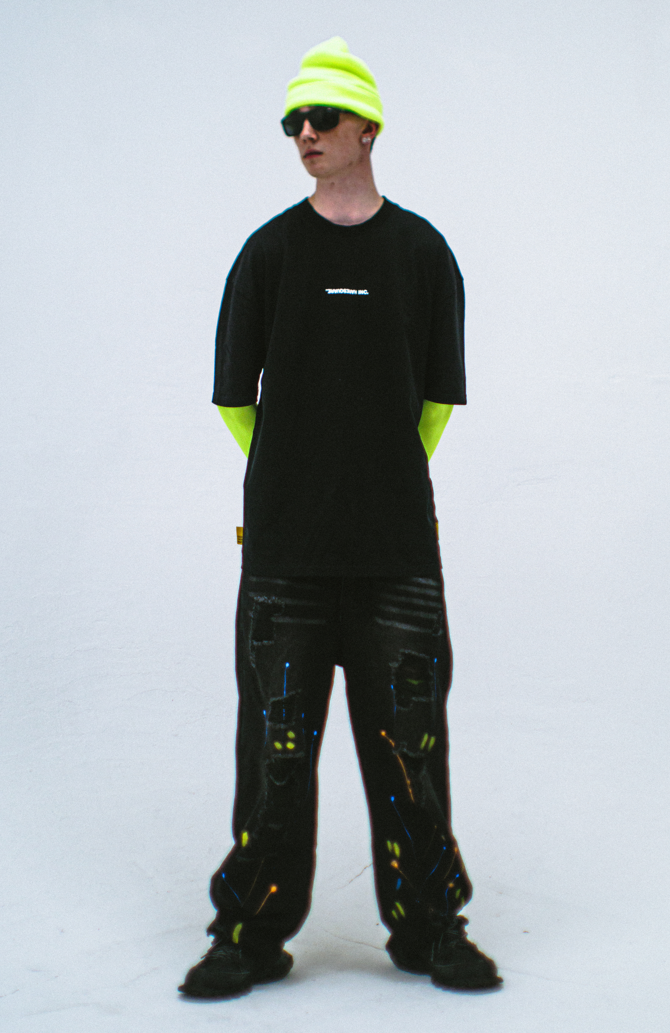 Model in the Haresquare Black T-shirt with a white print, styled with Haresquare paint splash black denim jeans and designer sunglasses – unisex luxury sportswear from Ireland.