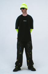 Model in the Haresquare Black T-shirt with a white print, styled with Haresquare paint splash black denim jeans and designer sunglasses – unisex luxury sportswear from Ireland.