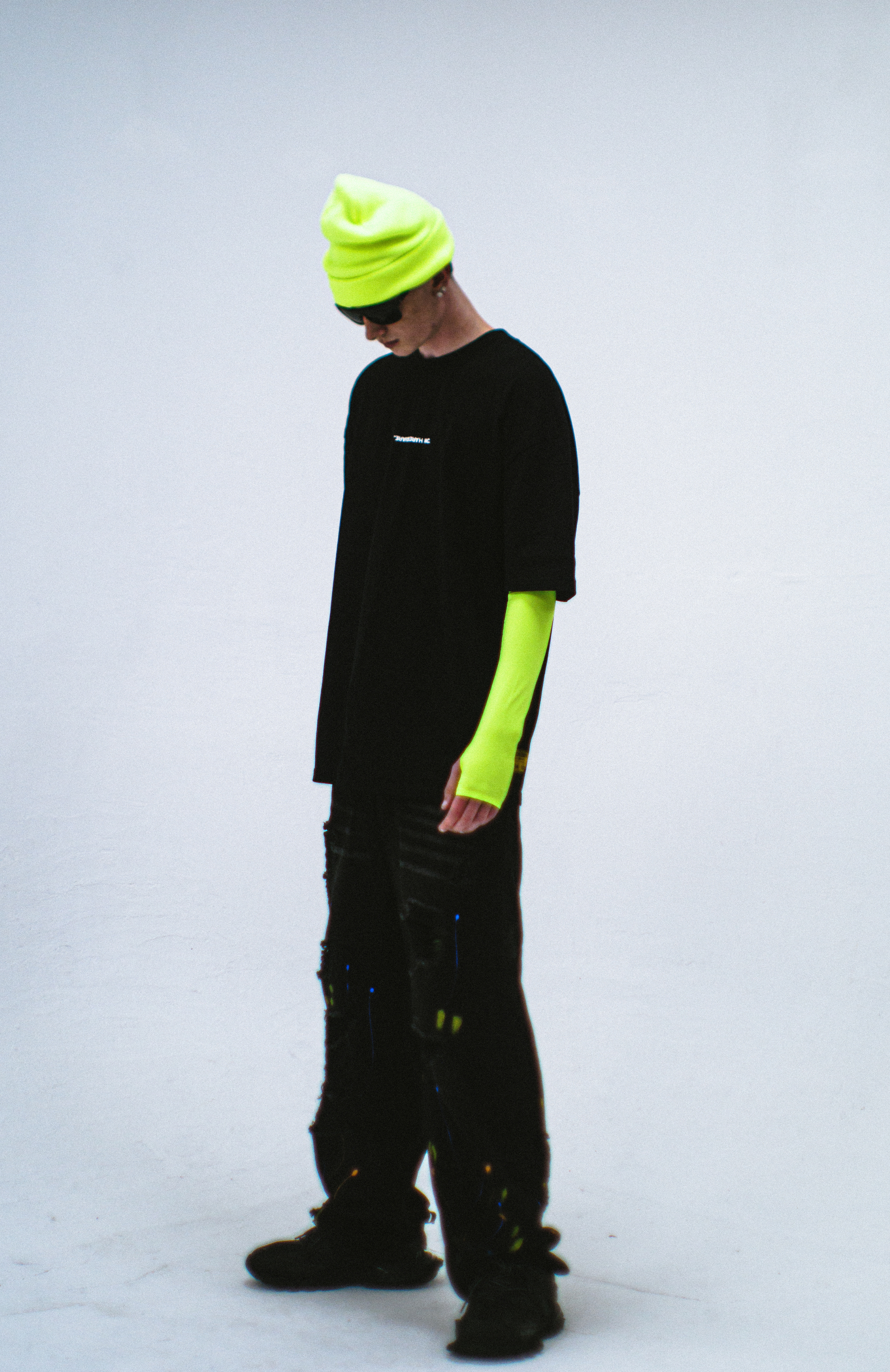 Model in the Haresquare Black T-shirt with a white print, styled with Haresquare paint splash black denim jeans and designer sunglasses – unisex luxury sportswear from Ireland.