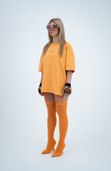 Model in the Haresquare Apricot Tan T-shirt with a grey print, styled with Haresquare mini skirt, designer sunglasses, and designer boots in orange – unisex luxury sportswear from Ireland.