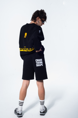Model in the Haresquare Superhuman black sweatshirt with yellow print, styled with Haresquare black shorts – unisex luxury streetwear from Ireland.