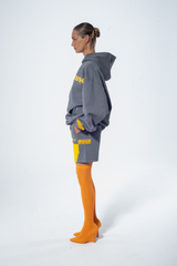 Model in the Haresquare Steey Grel Hoodie with a Yellow print, styled with Haresquare Grey shorts and orange designer boots – unisex luxury streetwear from Ireland.