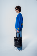 Model in the Haresquare Superhuman Nautical Blue sweatshirt with Yellow print, styled with Haresquare Blue denim jeans and haresquare bag – unisex luxury streetwear from Ireland.
