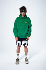 Model in the Haresquare Superhuman Abundant Green hoodie with yellow print, styled with Haresquare black shorts – unisex luxury streetwear from Ireland.