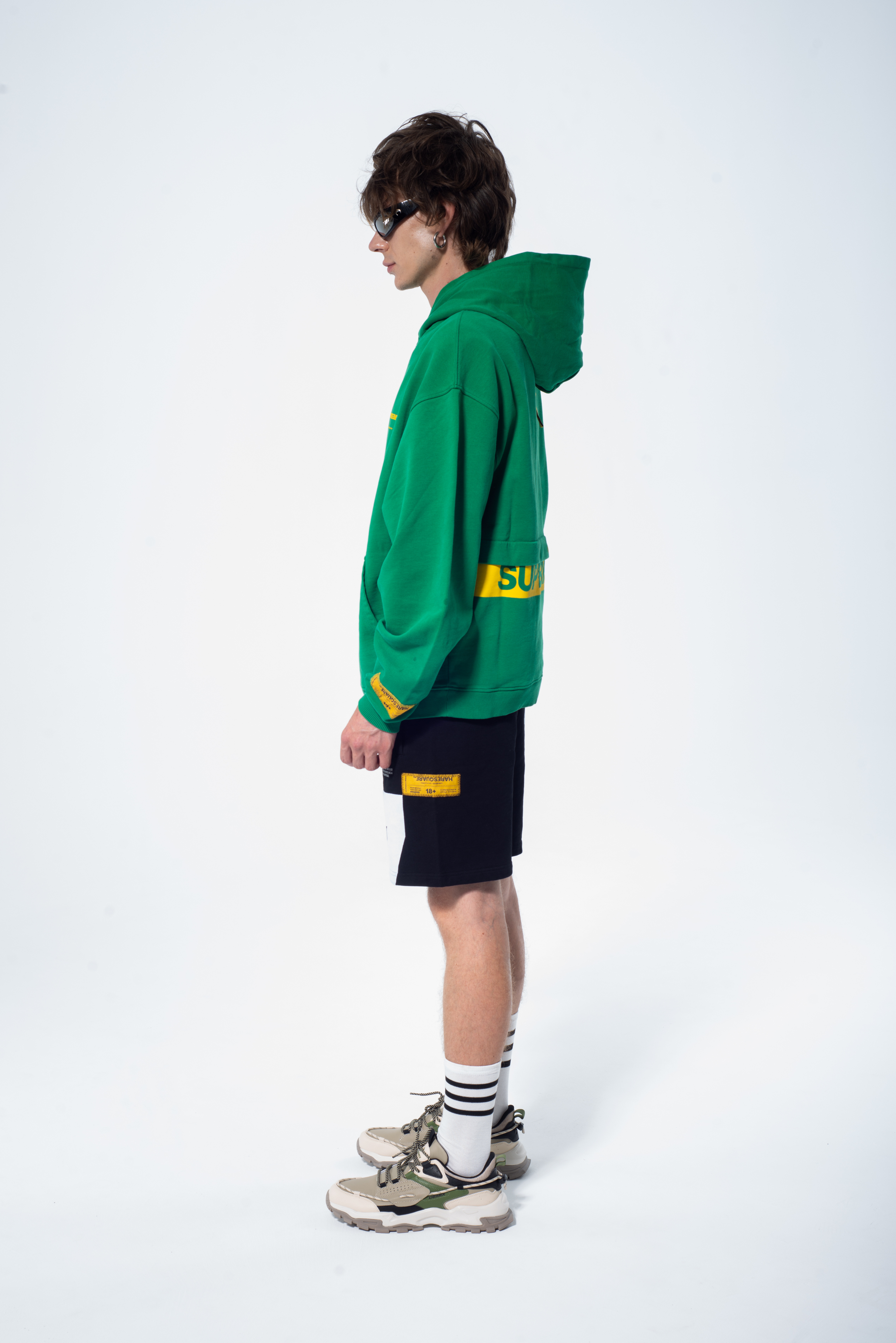Model in the Haresquare Superhuman Abundant Green hoodie with yellow print, styled with Haresquare black shorts – unisex luxury streetwear from Ireland.