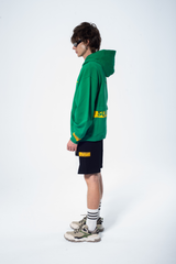 Model in the Haresquare Superhuman Abundant Green hoodie with yellow print, styled with Haresquare black shorts – unisex luxury streetwear from Ireland.
