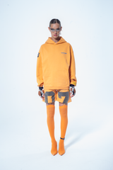 Model in the Haresquare Superhuman Apricot tan hoodie with Blue print, styled with Haresquare shorts – unisex luxury streetwear from Ireland.