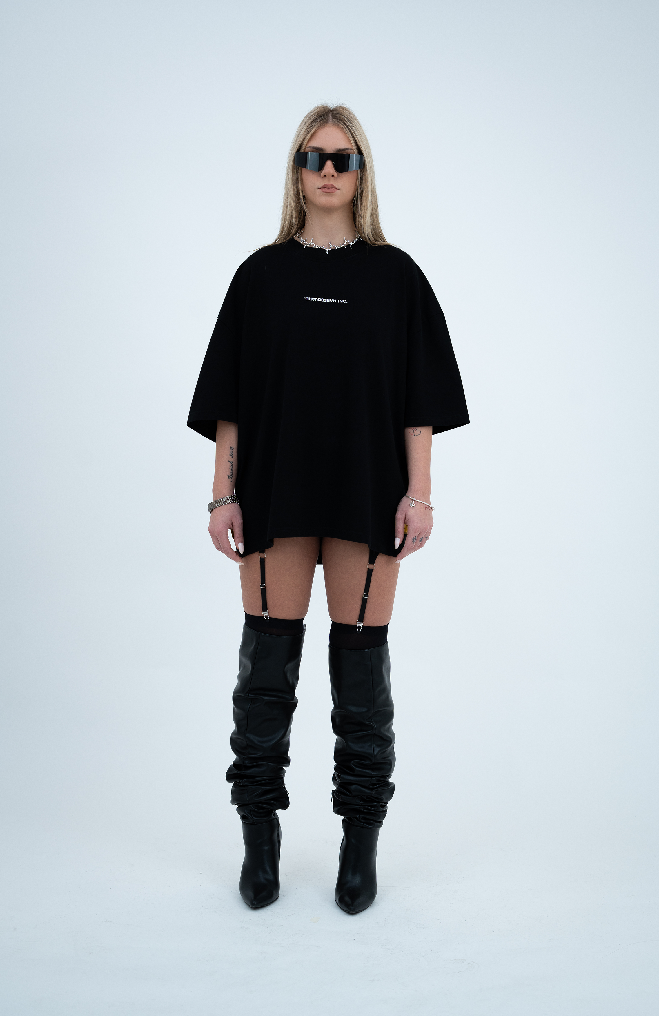 Model in the Haresquare Black T-shirt with a white print, styled with Haresquare mini skirt, designer sunglasses, and designer boots in black – unisex luxury sportswear from Ireland.