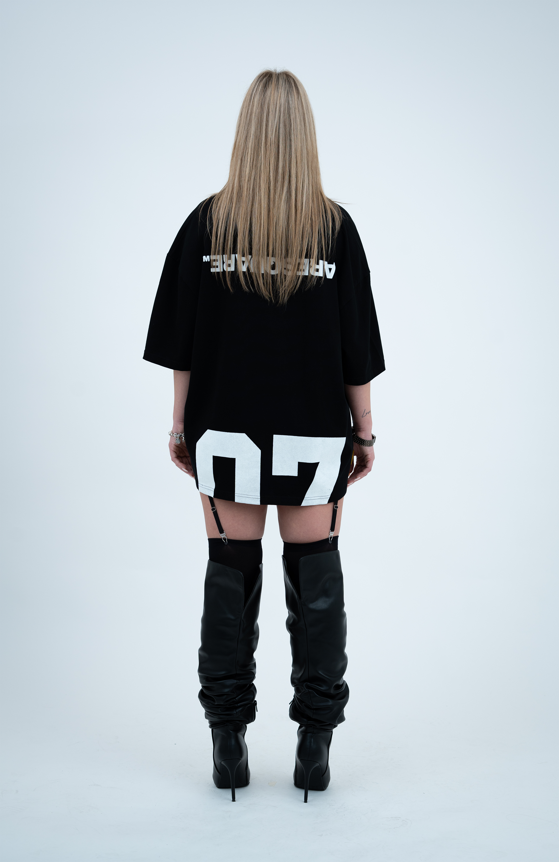 Model in the Haresquare Black T-shirt with a white print, styled with Haresquare mini skirt, designer sunglasses, and designer boots in black – unisex luxury sportswear from Ireland.