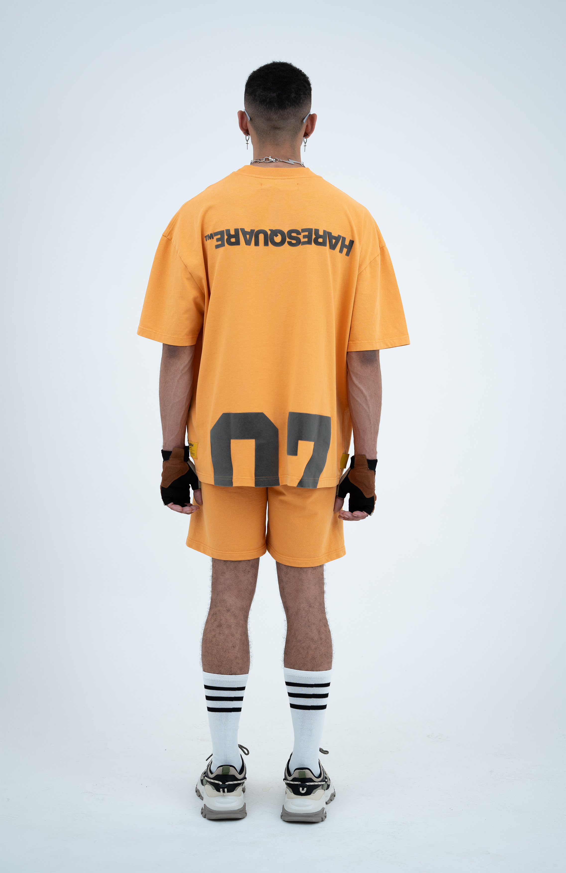 Model in the Haresquare Apricot Tan T-shirt with a grey print, styled with Haresquare Apricot Tan shorts and designer sunglasses – unisex luxury sportswear from Ireland.