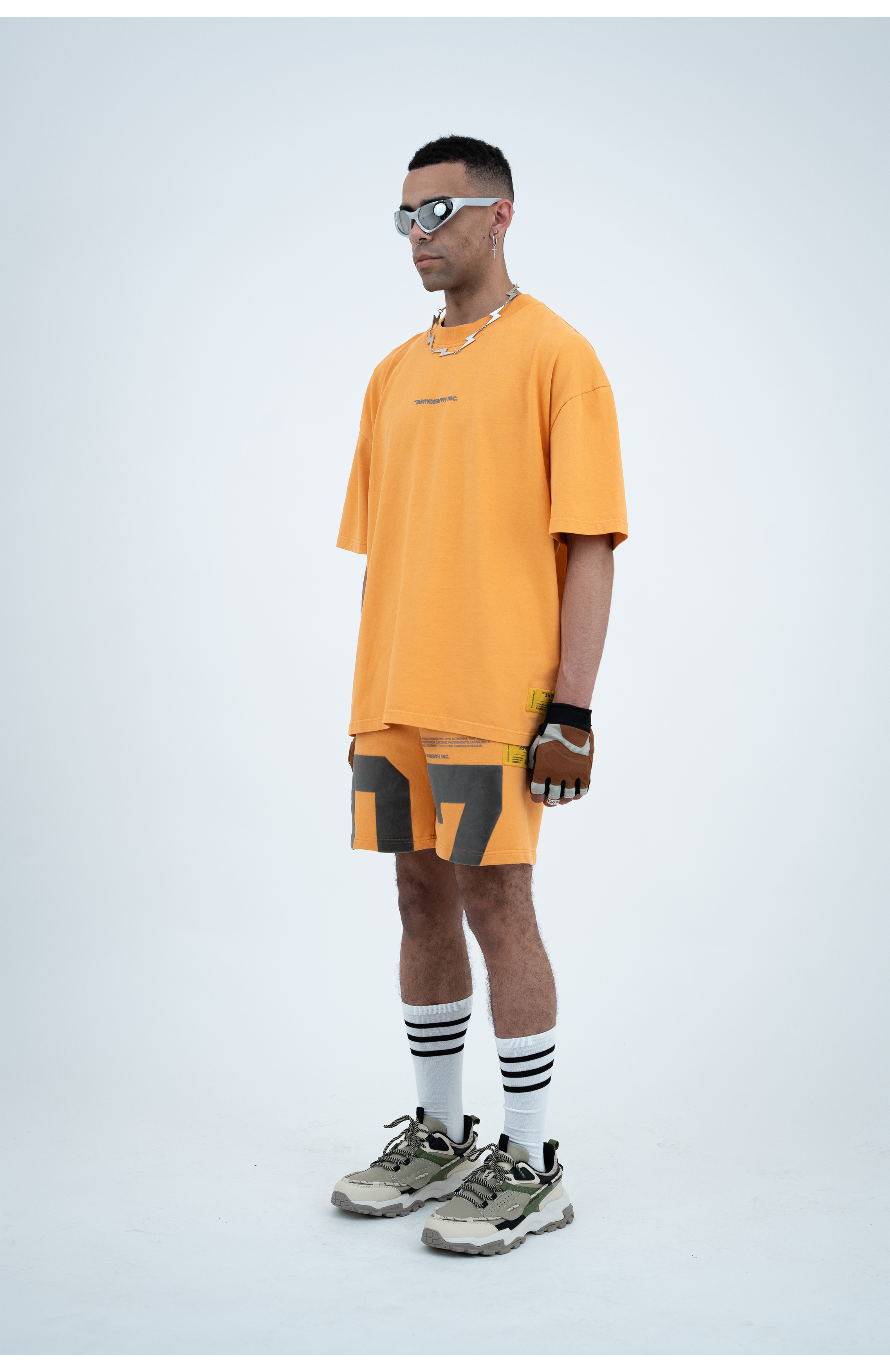 Model in the Haresquare Apricot Tan T-shirt with a grey print, styled with Haresquare Apricot Tan shorts and designer sunglasses – unisex luxury sportswear from Ireland.