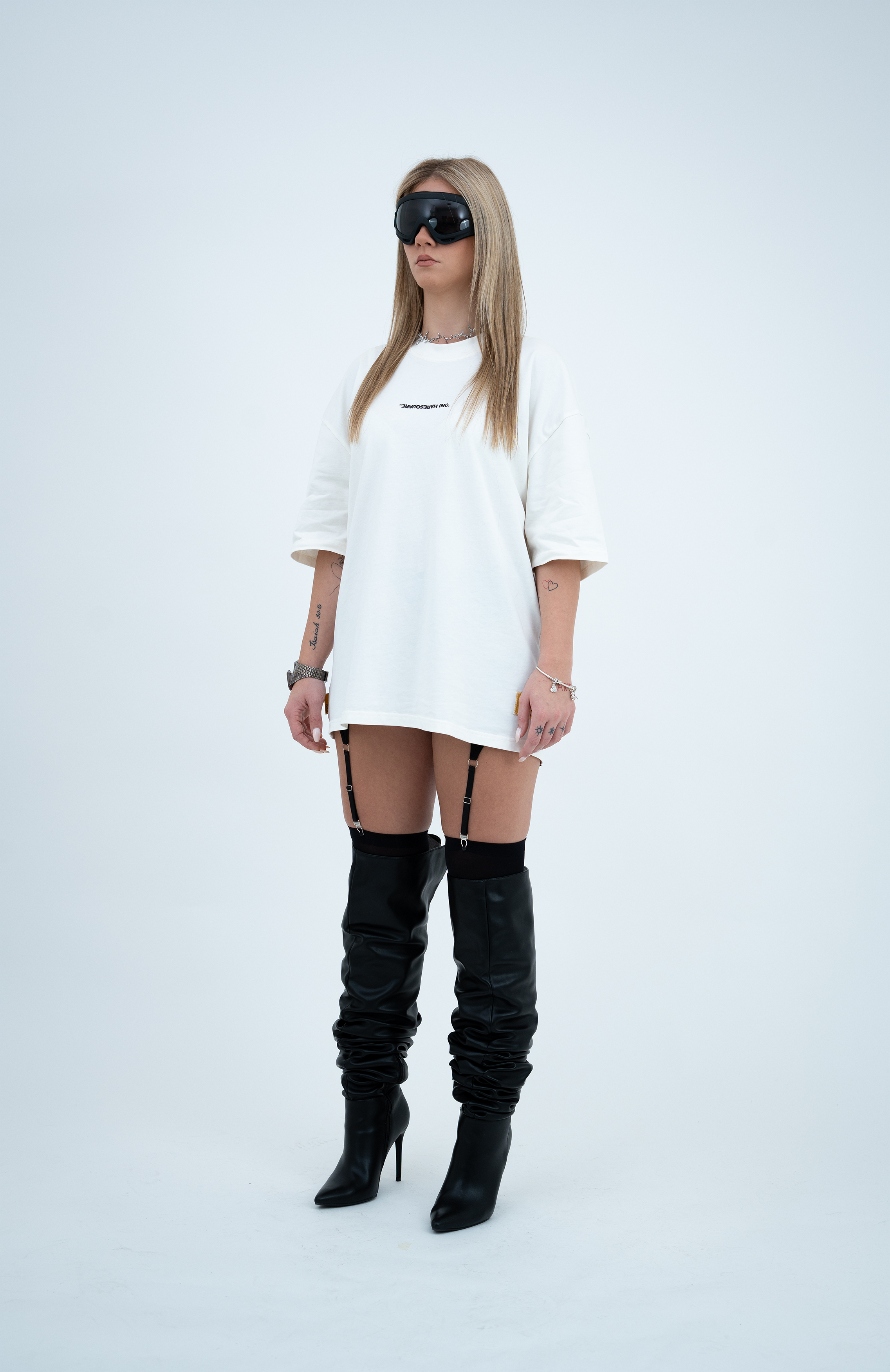 Model in the Haresquare Black T-shirt with a white print, styled with Haresquare mini skirt, designer sunglasses, and designer boots in black – unisex luxury sportswear from Ireland.