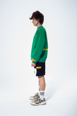 Model in the Haresquare Superhuman Abundant Green sweatshirt with Yellow print, styled with Haresquare black shorts – unisex luxury streetwear from Ireland.