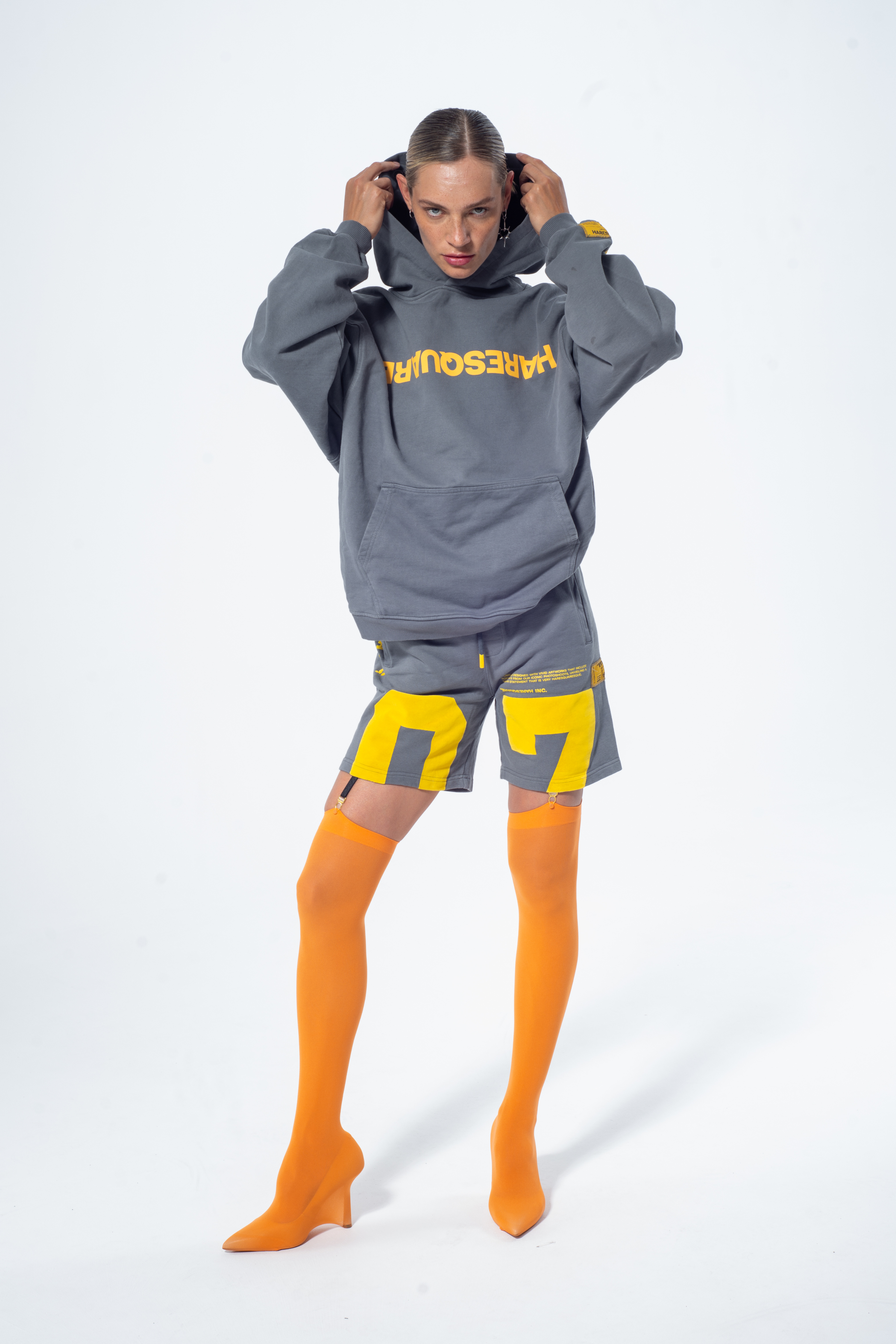 Model in the Haresquare Steel Grey Hoodie with a Yellow print, styled with Haresquare Grey shorts and orange designer boots – unisex luxury streetwear from Ireland.