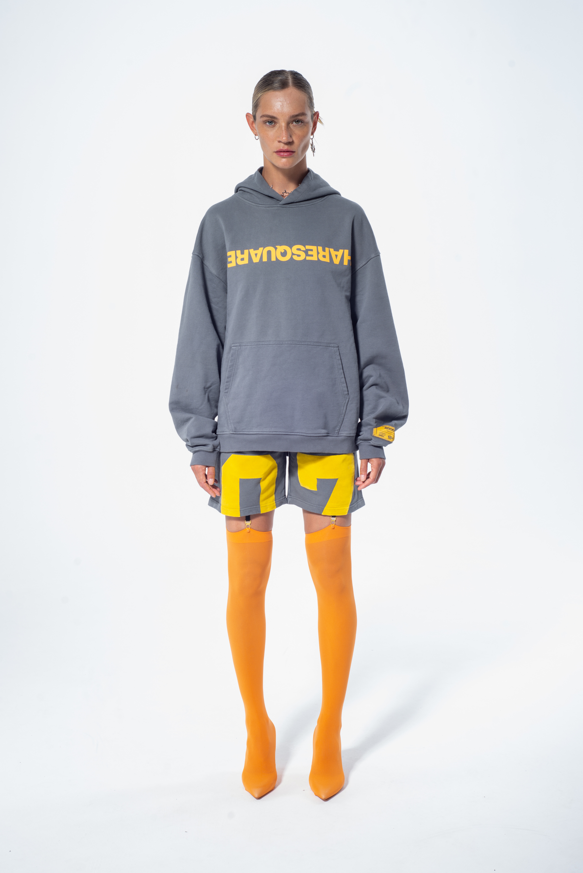 Model in the Haresquare Steel Grey Hoodie with a Yellow print, styled with Haresquare Grey shorts and orange designer boots – unisex luxury streetwear from Ireland
