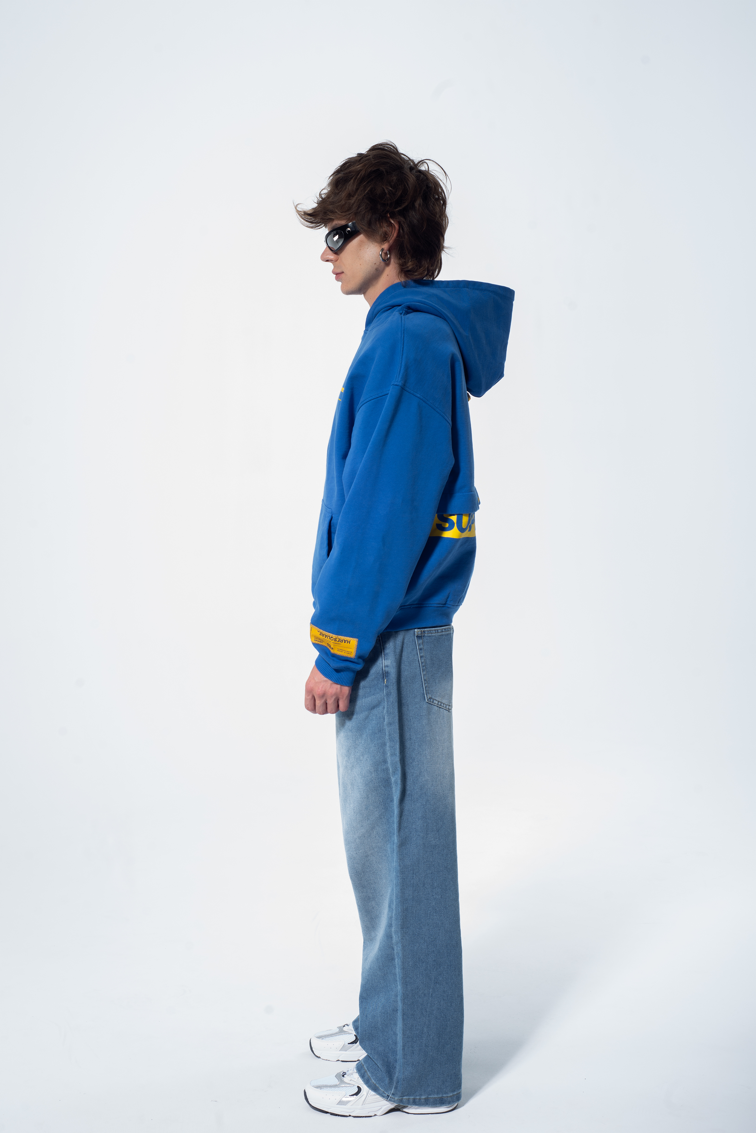 Model in the Haresquare Superhuman Nautical blue hoodie with yellow print, styled with Haresquare denim jeans – unisex luxury streetwear from Ireland.