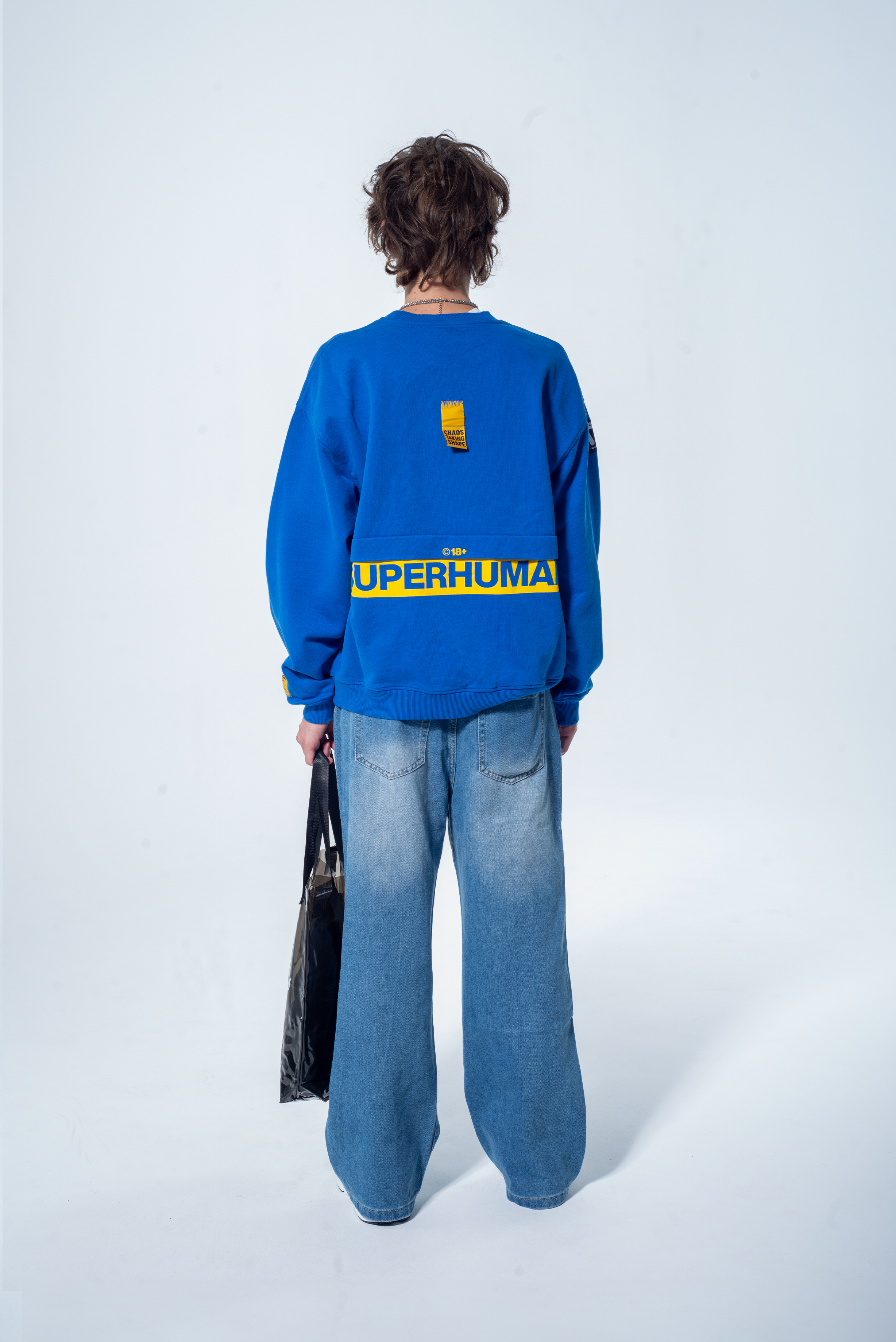 Model in the Haresquare Superhuman Nautical Blue sweatshirt with Yellow print, styled with Haresquare Blue denim jeans and haresquare bag – unisex luxury streetwear from Ireland.