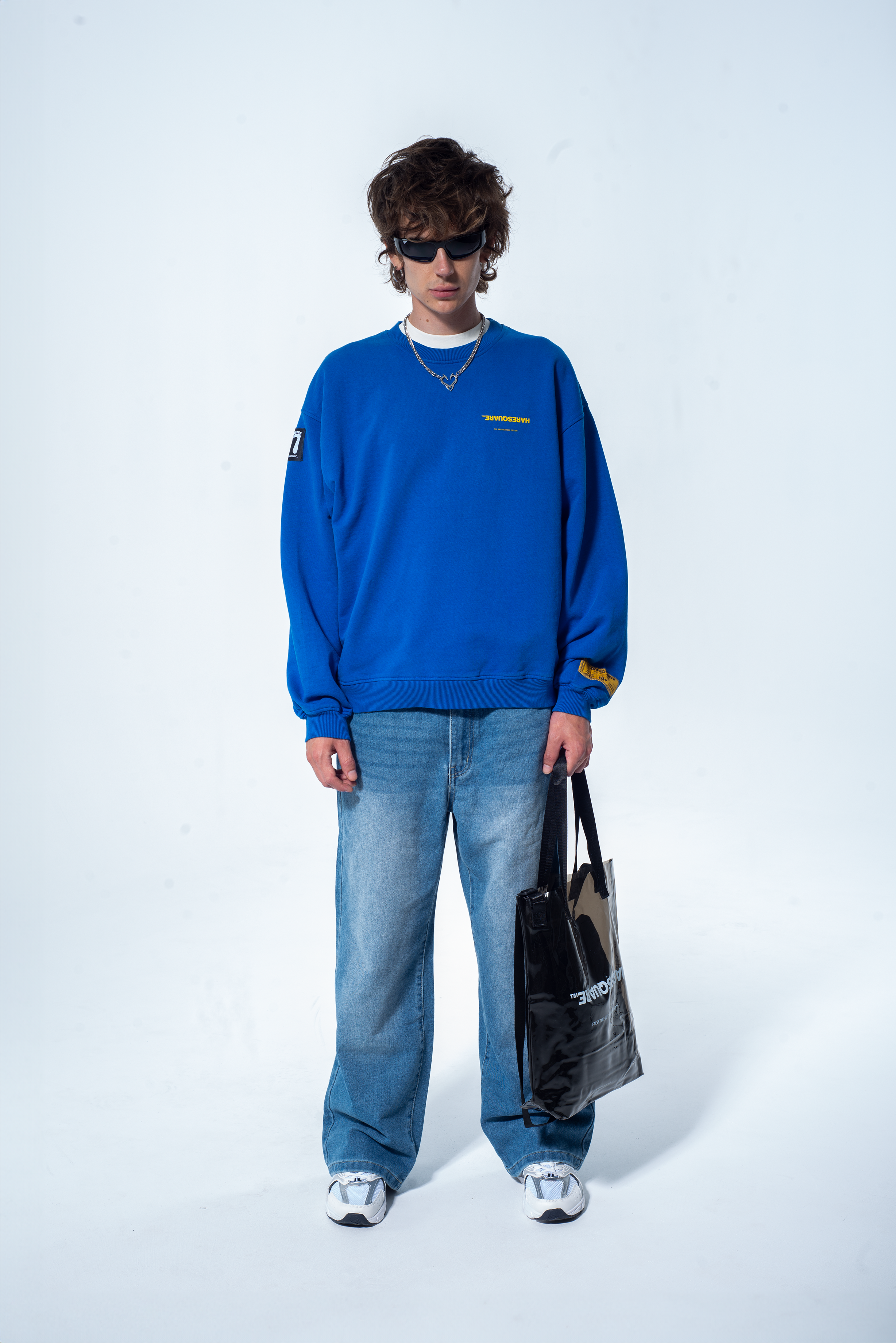 Model in the Haresquare Superhuman Nautical Blue sweatshirt with Yellow print, styled with Haresquare Blue denim jeans and haresquare bag – unisex luxury streetwear from Ireland.
