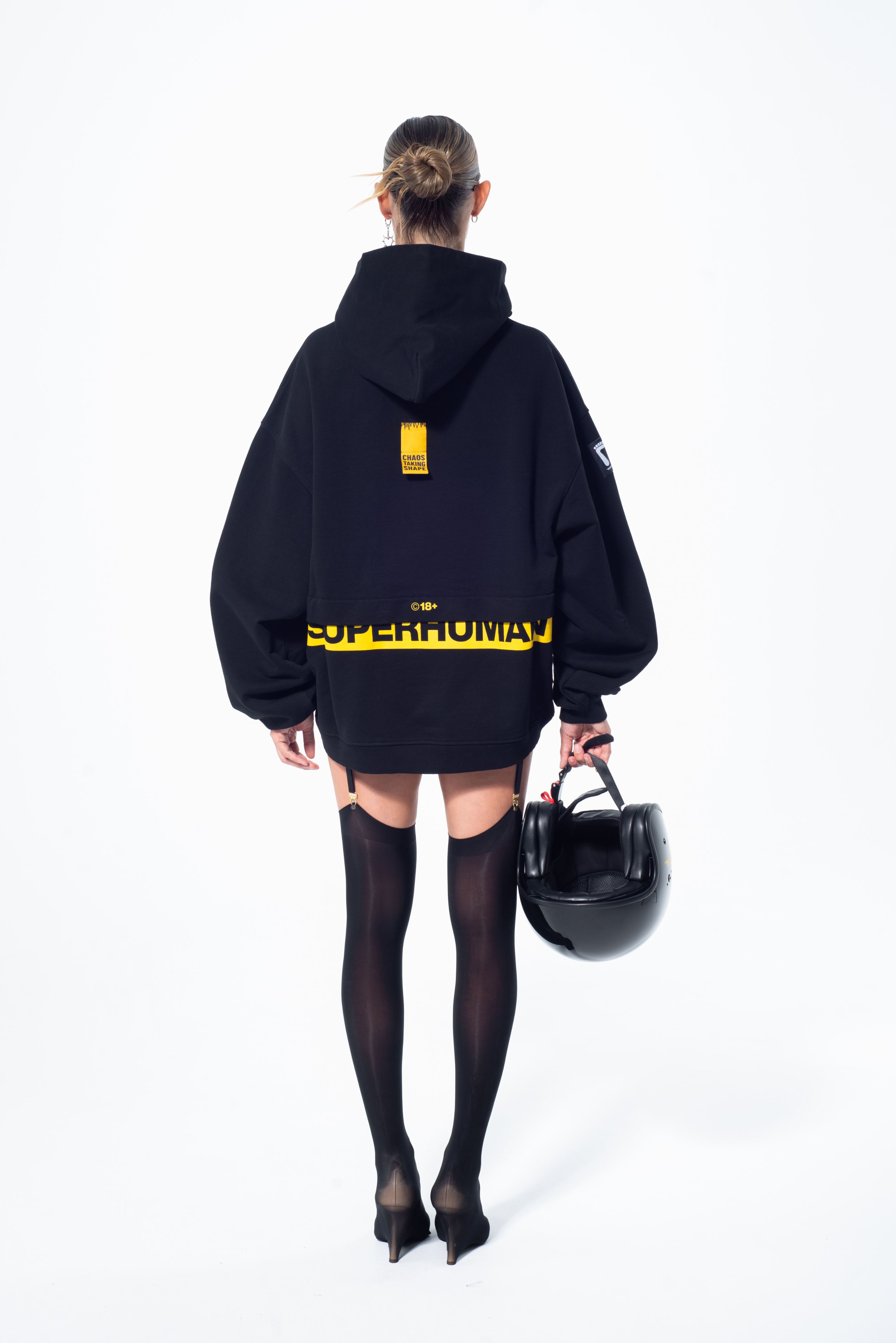 Model in the Haresquare Superhuman black hoodie with yellow print, styled with black helmet – unisex luxury streetwear from Ireland.