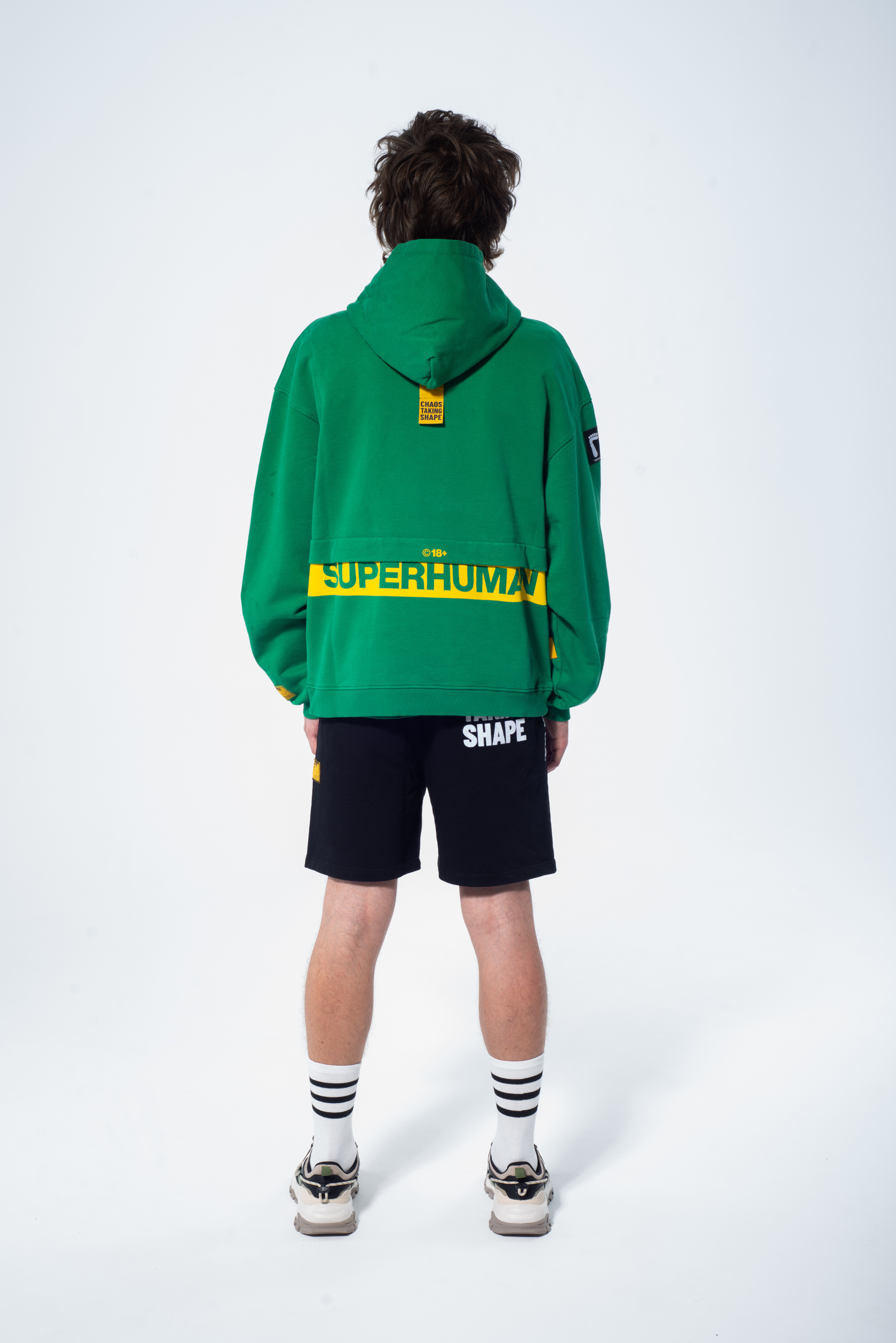 Model in the Haresquare Superhuman Abundant Green hoodie with yellow print, styled with Haresquare black shorts – unisex luxury streetwear from Ireland.
