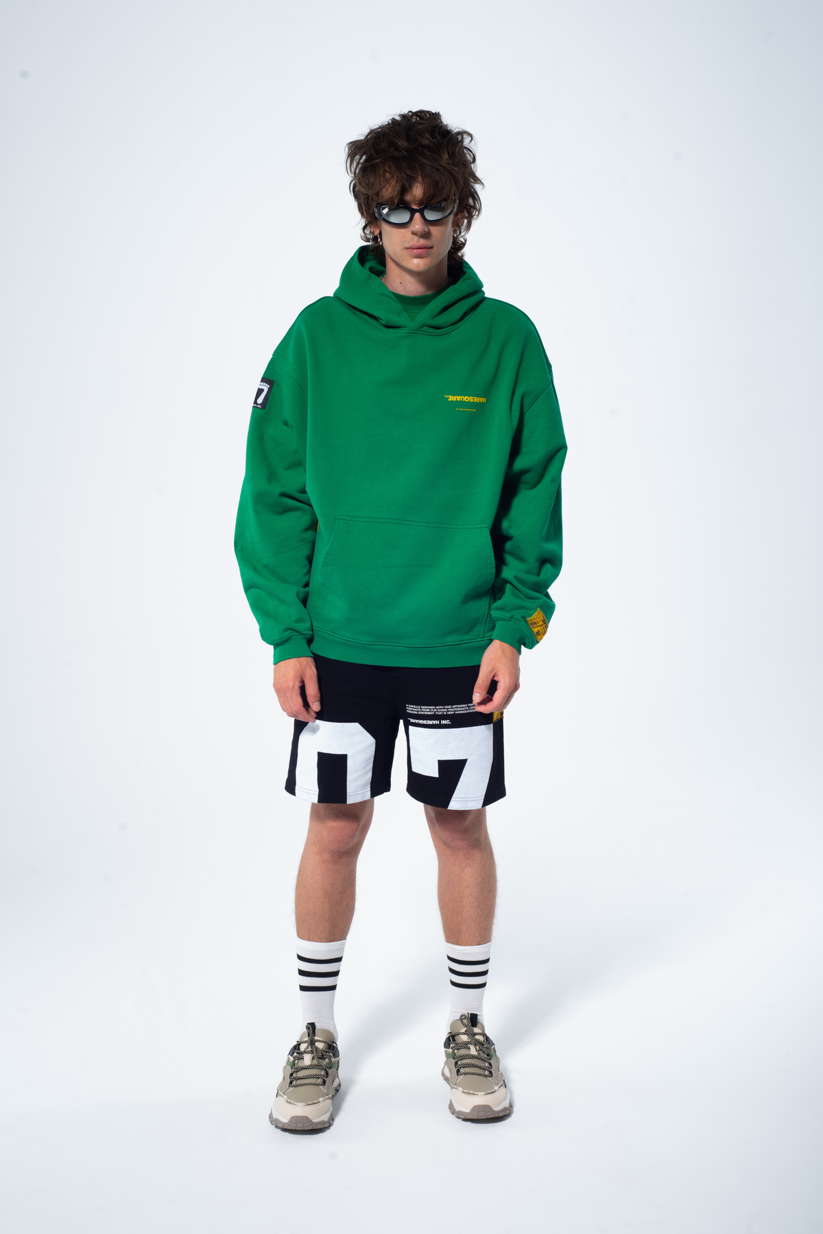 Model in the Haresquare Superhuman Abundant Green hoodie with yellow print, styled with Haresquare black shorts – unisex luxury streetwear from Ireland.