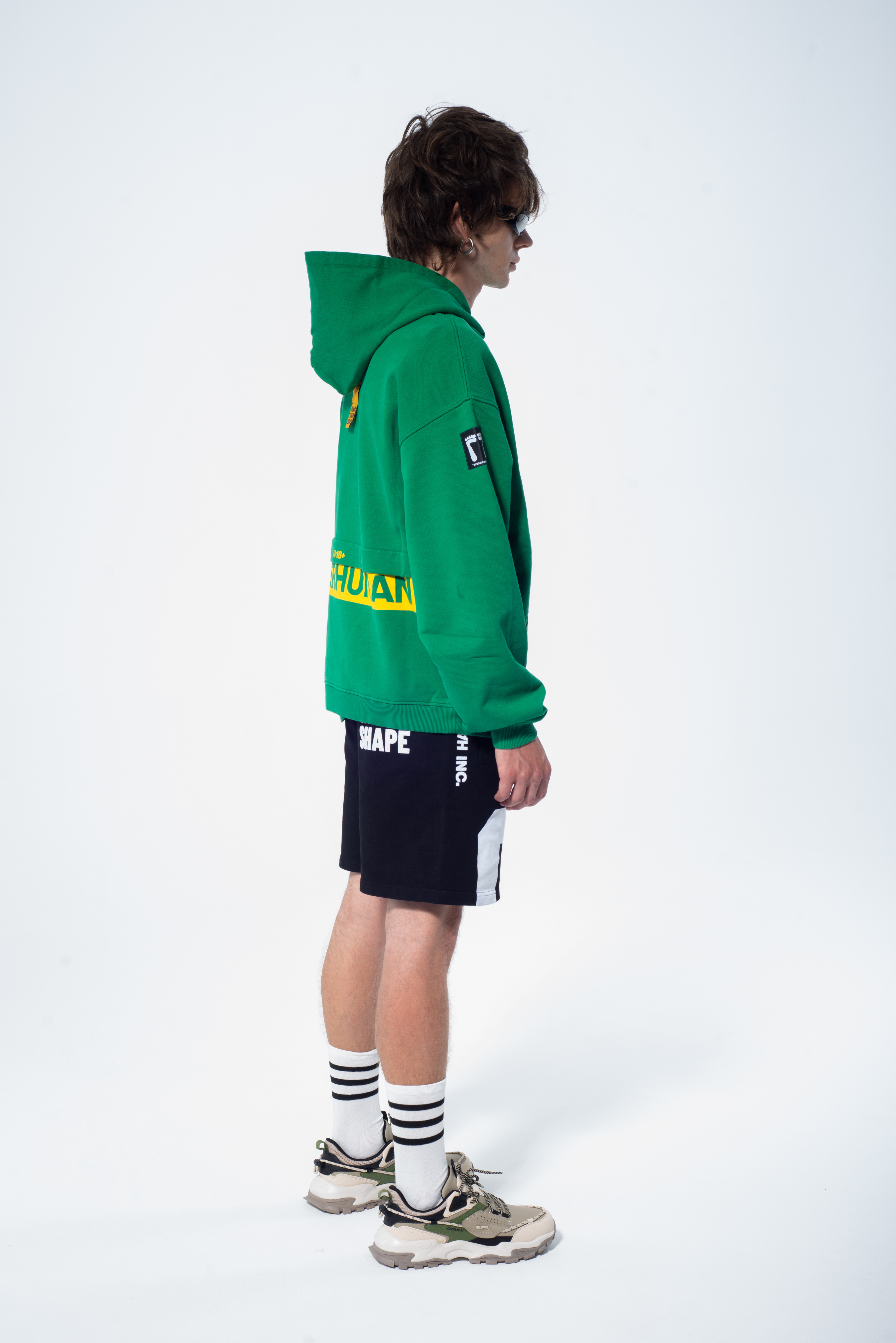 Model in the Haresquare Superhuman Abundant Green hoodie with yellow print, styled with Haresquare black shorts – unisex luxury streetwear from Ireland.